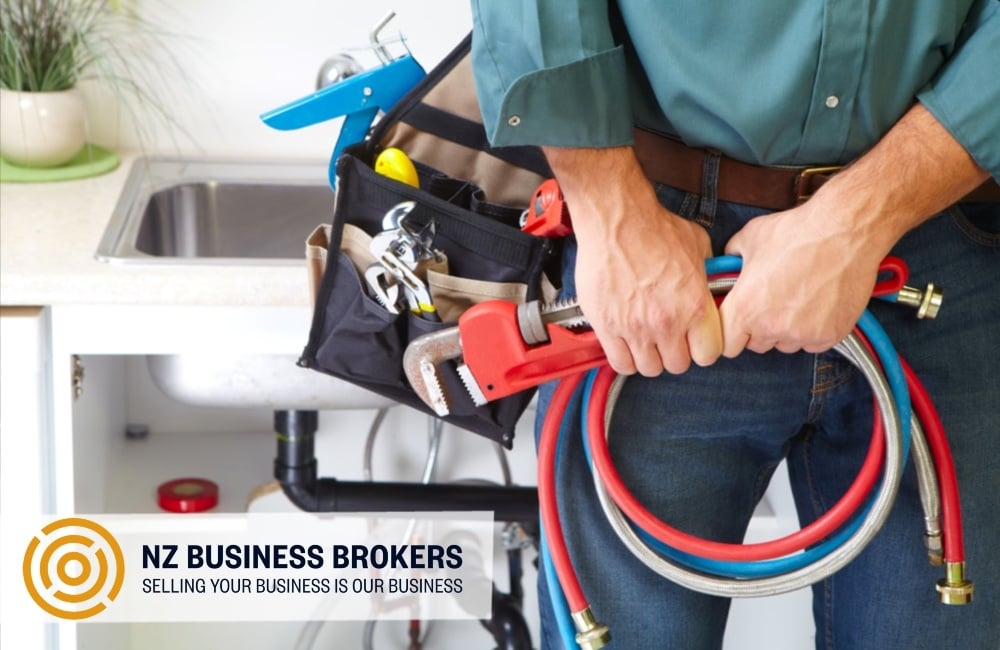 Plumber holding hoses and tools beside a kitchen sink